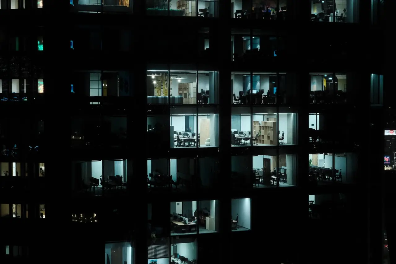 Façade vitrée d'un immeuble de bureaux la nuit, fenêtres éclairées en blanc froid