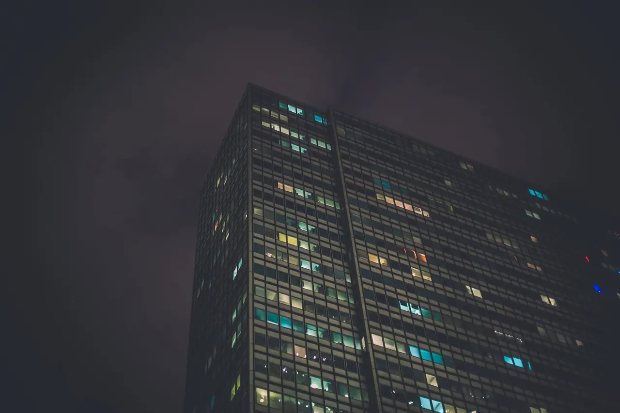 Contre-plongée d'une tour de bureaux dans la brume nocturne, fenêtres éclairées