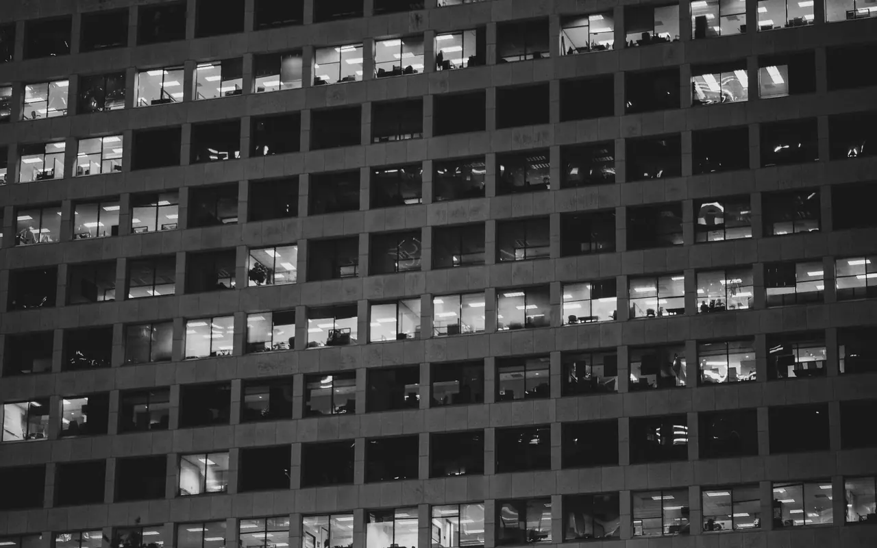 Façade d'un immeuble de bureaux en noir et blanc, rangées de fenêtres allumées la nuit