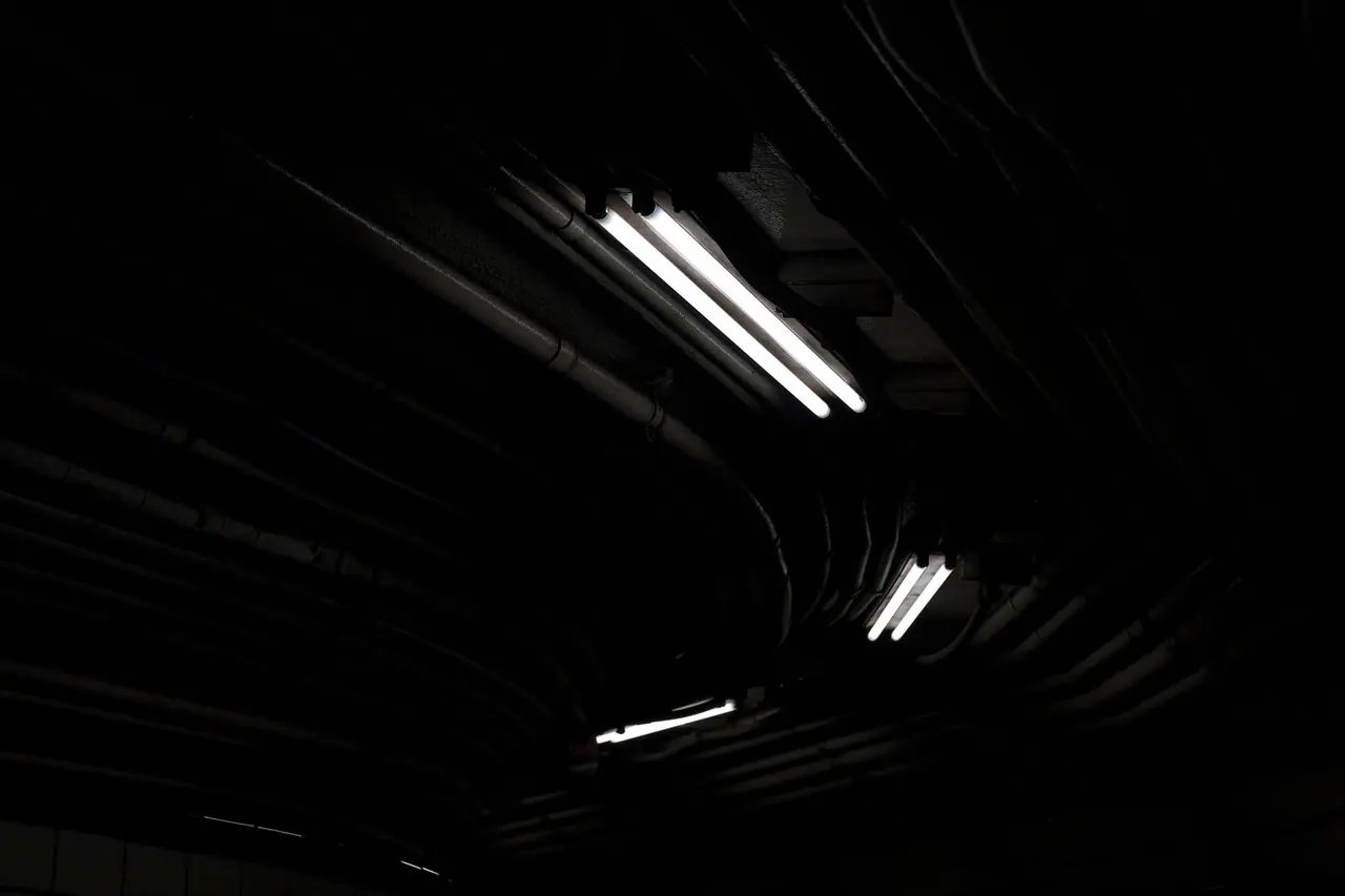 Plafond sombre avec tubes fluorescents et chemins de câbles dans l'obscurité