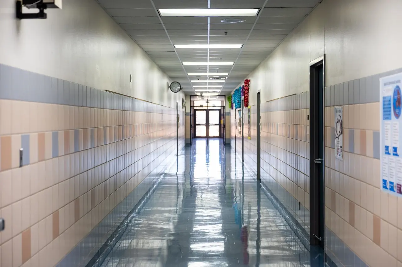 Couloir d'école aux murs carrelés et au sol brillant éclairé par des tubes